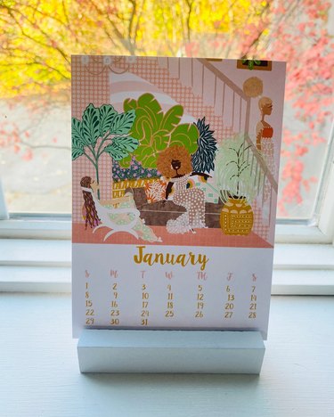 A calendar page for January 2023, featuring vibrant shades of pink, green and blue and a drawing of a dark-skinned woman sitting on a brown couch
