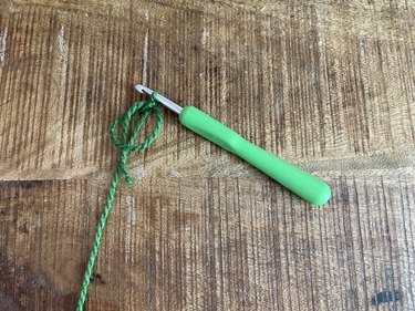 A magic crochet circle made out of green yarn and a green crochet hook