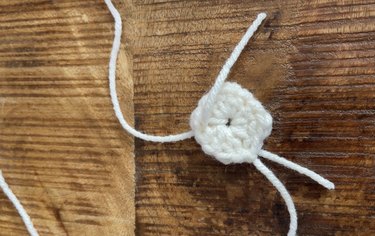 A white crochet square with a piece of yarn going through the corner