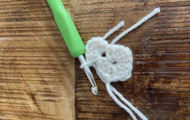 A white crochet square with a green crochet hook