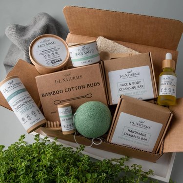 A cardboard box filled with eco-friendly self-care and skincare items, including a shampoo bar, cotton buds, a cleansing bar, face mask, face salve, hair serum, lip balm and deodorant.