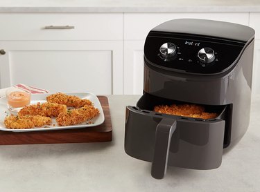Instant Essentials 4-Quart Air Fryer Oven in black next to plate of air-fried chicken tenders.
