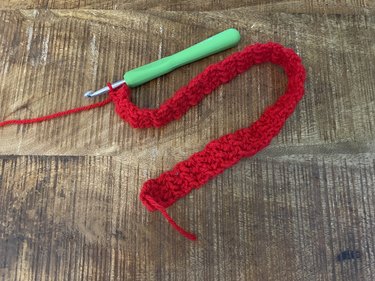 A long, thin crochet rectangle made from red yarn.