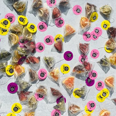 An assortment of cocktail infusions bags filled with fruits and herbs. Half the bags have yellow tags, half have pink tags.