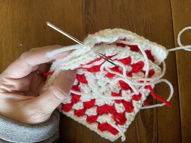 Two red and white granny squares being stitched together with white yarn