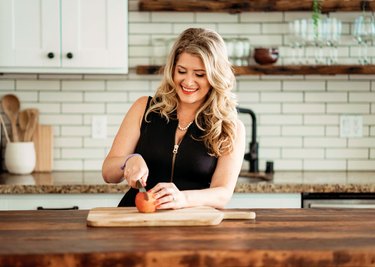 A woman in a black top with blond hair cuts an apple on a wood cutting board