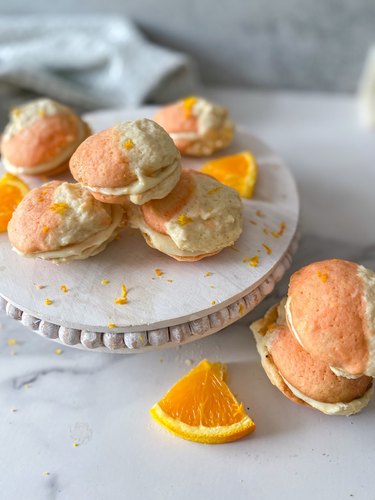 A pile of orange and white Dreamsicle cookies sit atop a white tray surrounded by a few orange slices