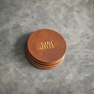 A stack of light brown leather coasters with "JWM" stamped into the center.
