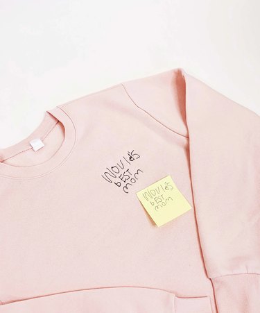 A light pink sweatshirt with "World's Best Mom" embroidered in children's handwriting.