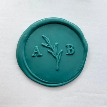 A teal blue wax stamp with the letters "A" and "B" on either side of a small branch.