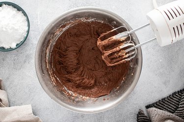 Hot chocolate powder and powdered sugar in a bowl with a mixer hovering.