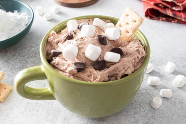 Hot cocoa dip and a graham cracker in a green mug.