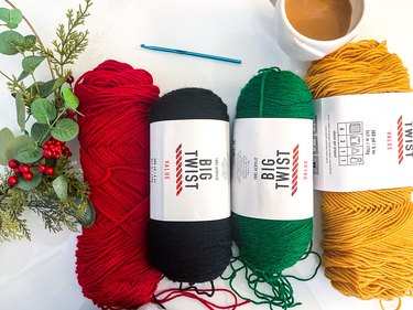 Red, black, green and yellow yarn on a table with a crochet hook and coffee mug