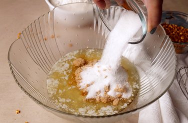 Pouring sugars into a large mixing bowl that has melted butter