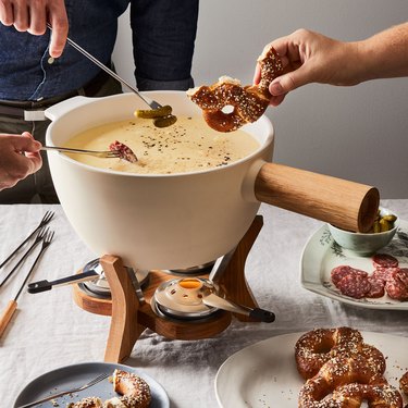 People sharing an extra-large fondue set with a white ceramic bowl and a wooden handle and base.
