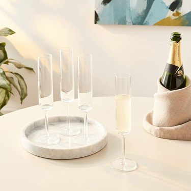 Square shaped champagne flutes on a marble tray next to a bottle of Champagne on a countertop.