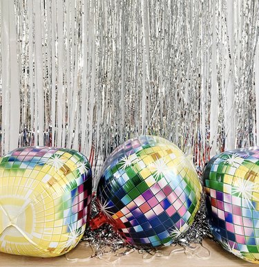 Colorful disco ball balloons against a silver tinsel backdrop.