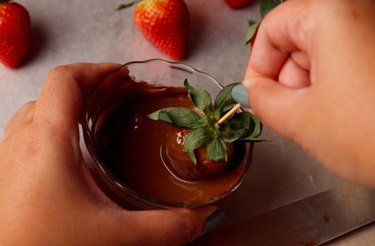 Dipping a strawberry into a bowl of melted chocolate.