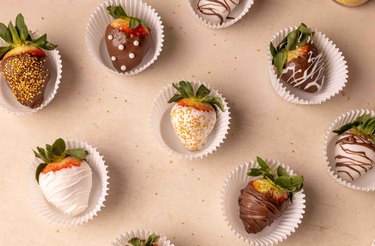 Fancy chocolate-covered strawberries in cupcake liners on a backdrop.