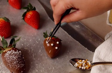 Using tweezers to add sprinkles on chocolate-covered strawberry.