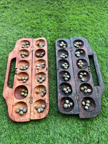 A set of two wood mancala boards on green grass