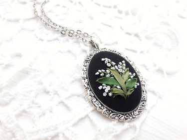 Embroidered lily of the valley flowers on a black pendant and silver chain.