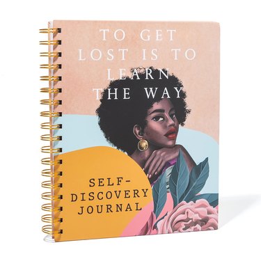 A self-discovery journal featuring a Black woman with an Afro hairstyle, flowers, soft colors and the phrase "To Get Lost Is to Learn the Way"