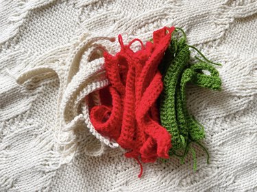 A pile of red, green and white crochet strips each made from two rows of 30 double crochet stitches.
