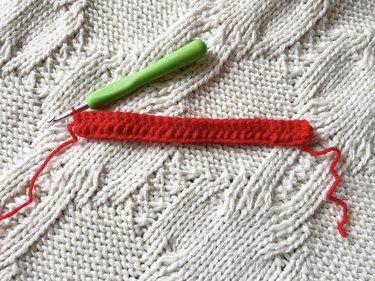 Two rows of 30 double crochet stitches made up of red yarn with a green crochet hook next to it.