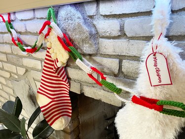 A closeup of three Christmas stockings hanging above a gray brick fireplace with a red, green and white chain garland.