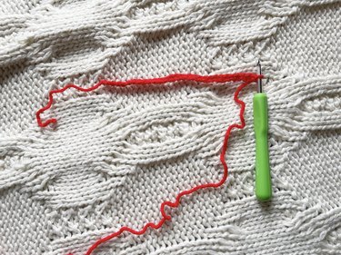 A row of 31 crochet stitches made up of red yarn with a green yarn hook next to it.