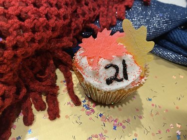 A cupcake with white frosting, two paper leaf wafers and the number 21 written in black.