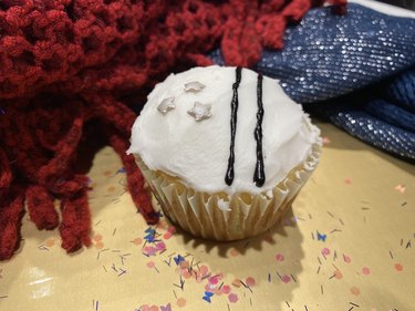A white cupcake with two black lines and three silver stars.