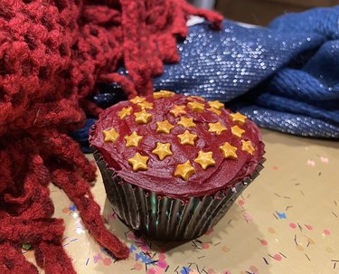 A cupcake with deep red (maroon) frosting and a smattering of gold candy stars.