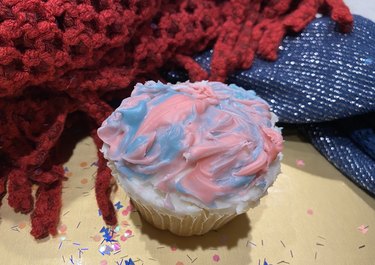 A cupcake with melted pink and blue swirled candy topping.