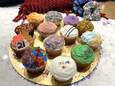 A gold platter with 13 cupcakes in vibrant shades with glitter strewn on the counter.