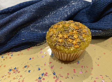 A cupcake with gold frosting, gold star candies and gold sprinkles.