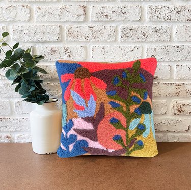 A vibrant, abstract punch needle pillow with botanical designs.