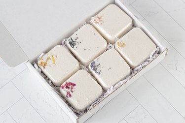 A box of six square bath bombs topped with flower petals and colorful infusions.