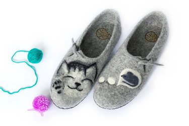A pair of gray felted wool slippers featuring a sleeping cat and a mouse.