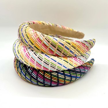 A set of three handwoven grass and raffia headbands with rainbow stripes.
