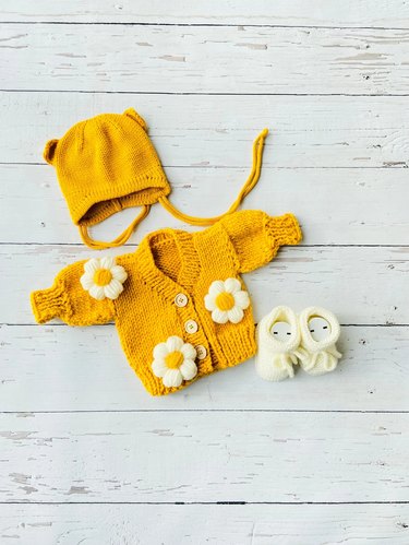 A bright yellow cardigan with sewn-on daisies and a matching yellow drawstring hat.