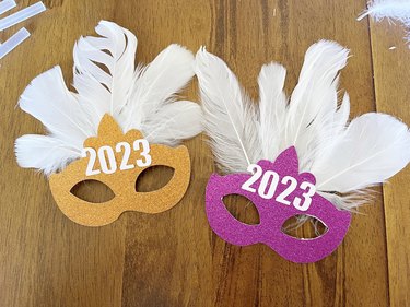 Pink and orange New Year's Eve masks with white feathers and "2023" on top.