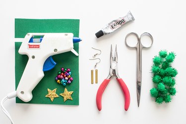 Glue gun, pliers, earring supplies, baubles, scissors, super glue and mini green pom poms.