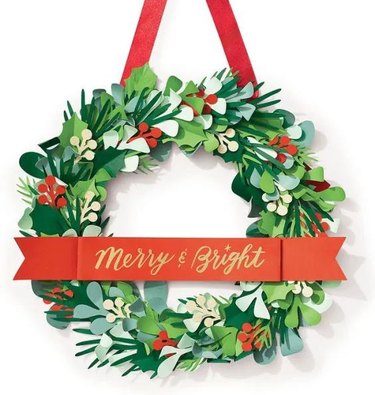 Paper craft 15-inch wreath with paper greeenery and a banner in the middle that reads "Merry & Bright"