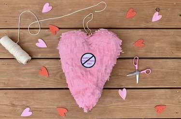 Heart piñata against a wooden background with scattered hearts and craft supplies