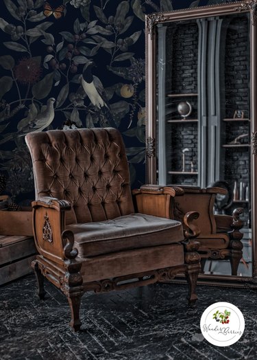 Vintage chair sitting in front of dark wallpaper featuring birds and plants