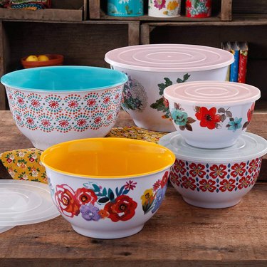 Set of Pioneer Woman mixing bowls with lids, on a rustic wooden tabletop