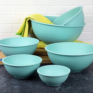 Teal mixing bowls on a dark grey counter, with a white subway tile bascksplash behind