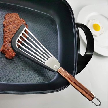 Fish spatula with silicone edge, shown in a non-stick pan with a fried egg in the background